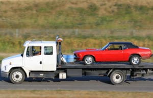 How Does Bring a Trailer Work 3 a red vintage car that was purchased through eBay motors being transported on a white truck driving on the highway